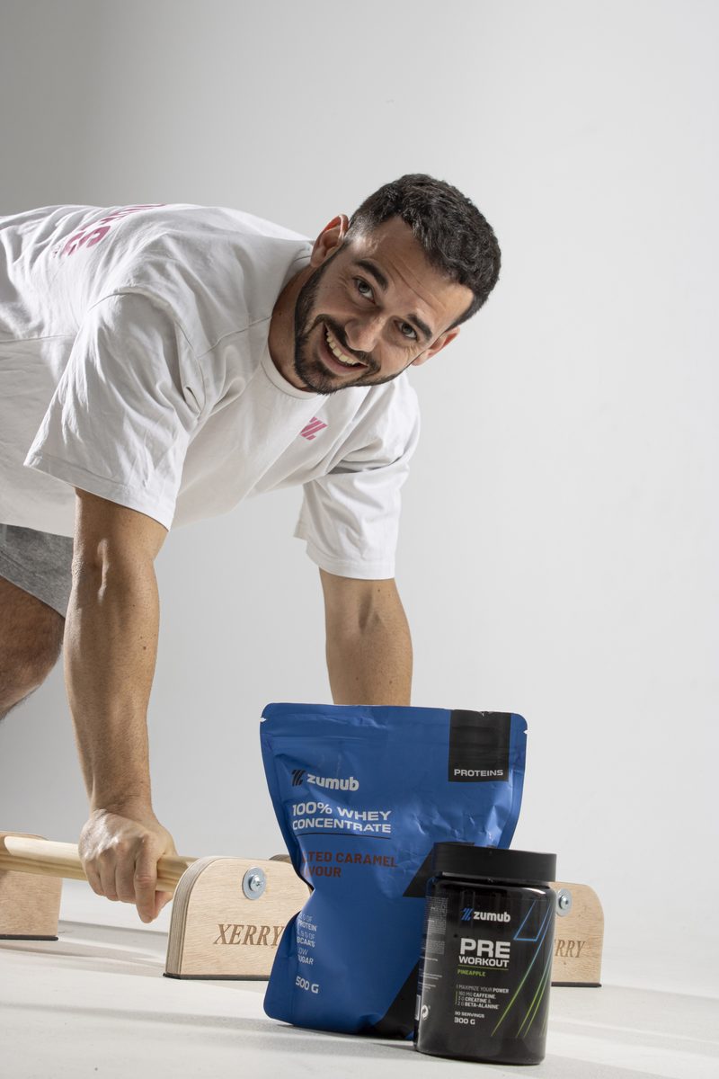 Iván apoyado en unas paralelas junto a la proteína y el pre-entreno que usa